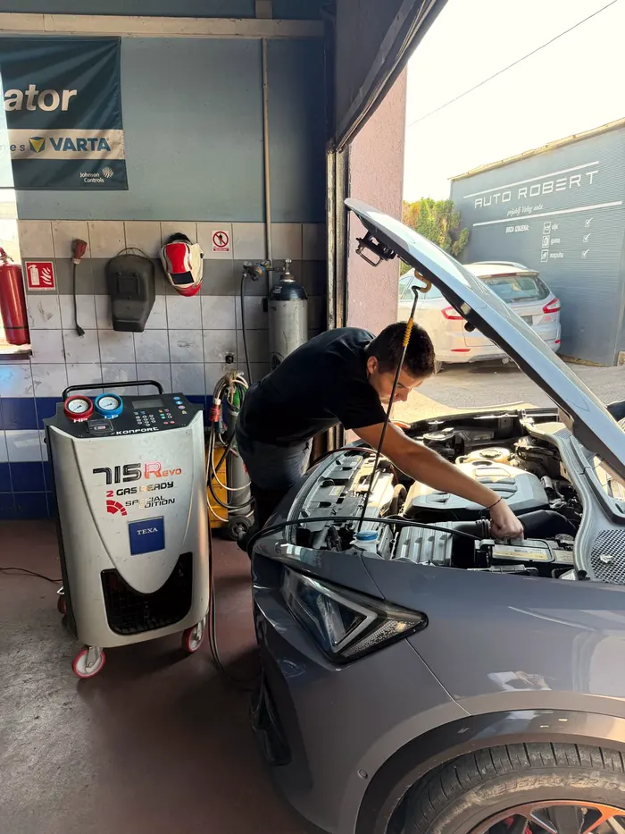 Mehaničar radi na motoru sivog automobila, pored njega TEXA Konfort 715R uređaj za servis klime