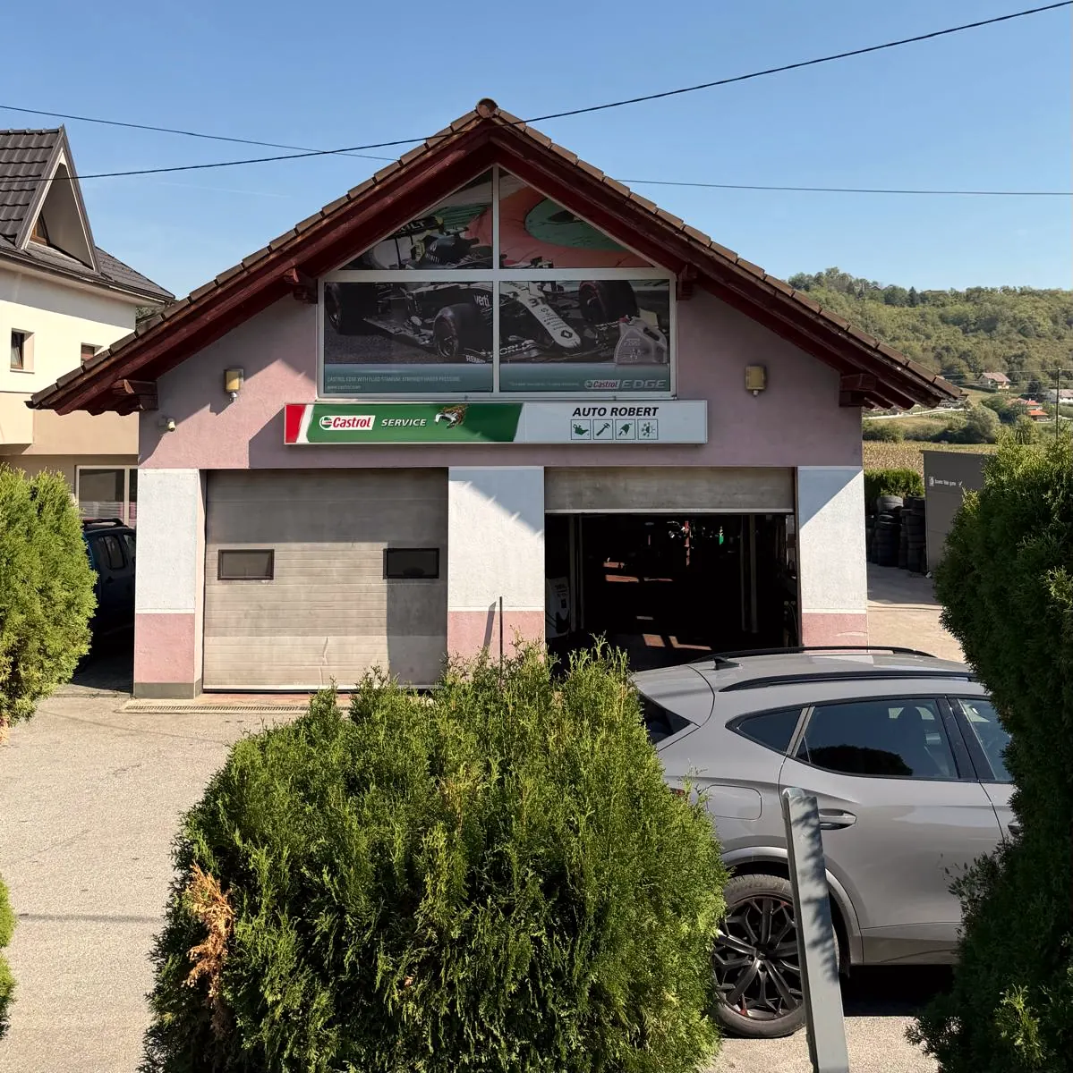 Pročelje radionice Auto Robert s natpisom Castrol Service i dvoja garažna vrata, iza brda Zagorja